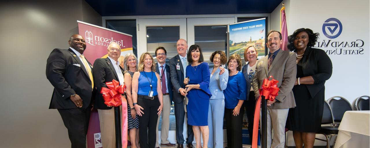 GVSU and Jackson College presidents and deans cutting red ribbon in front of GVSU office